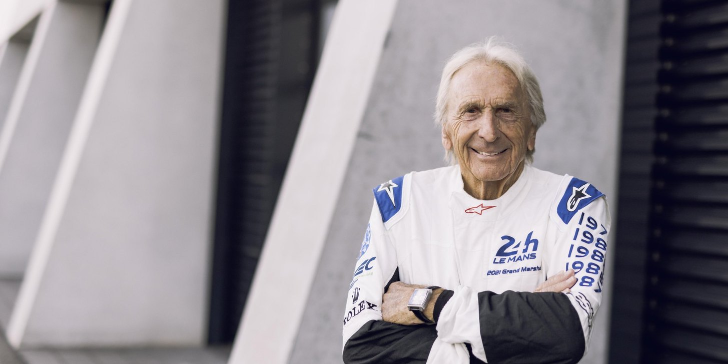 Derek Bell im weißen Rennoverall mit verschränkten Armen